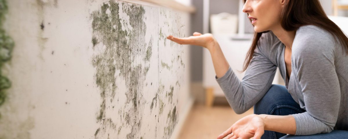 Frau zeigt auf Schimmel und Feuchtigkeit an der Wand im Haus
